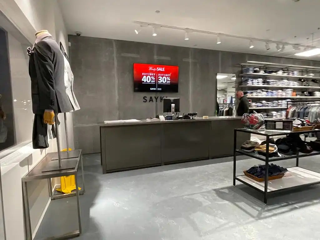 Modern retail checkout counter with a digital display screen mounted above it.